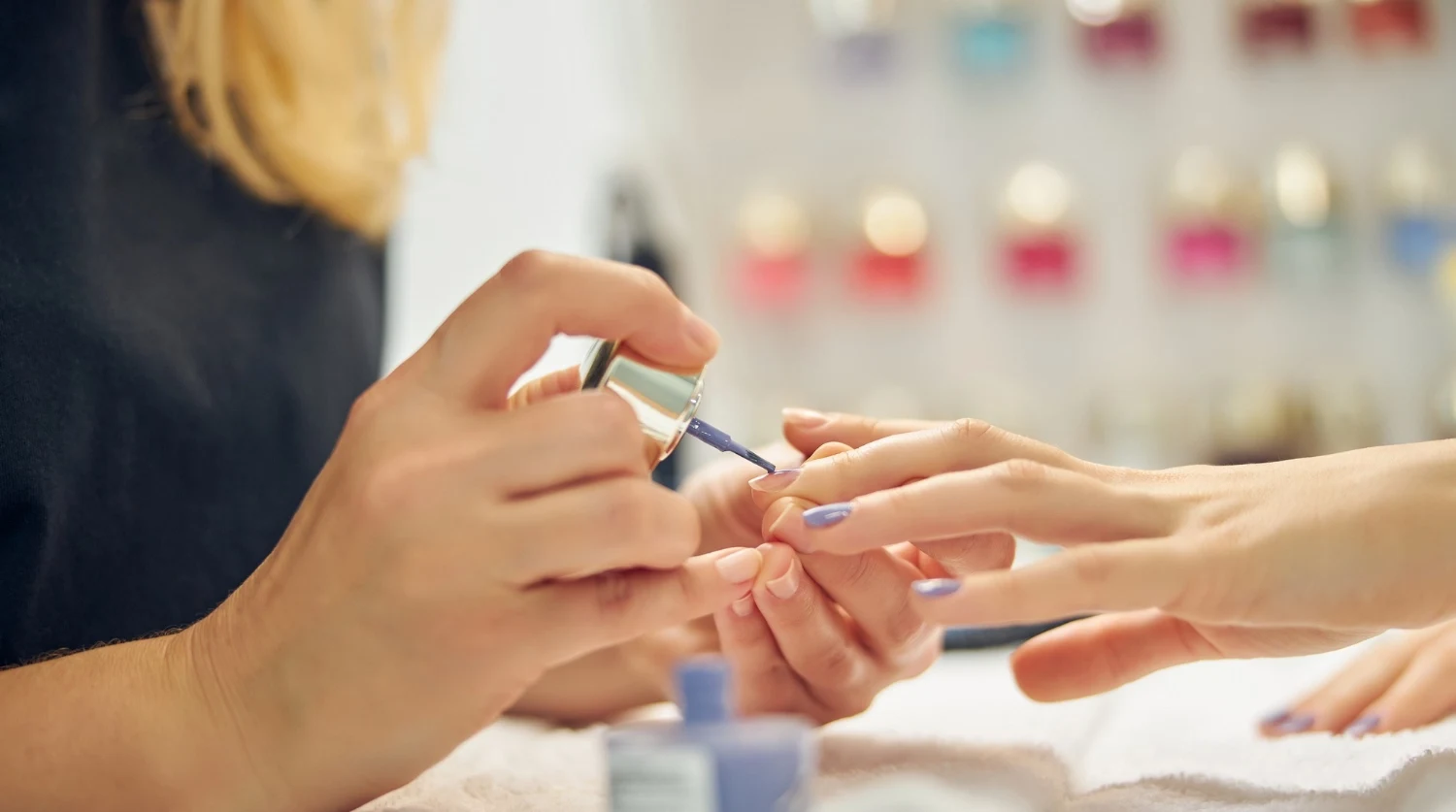 Manicurist applying lavender polish to a client’s nails